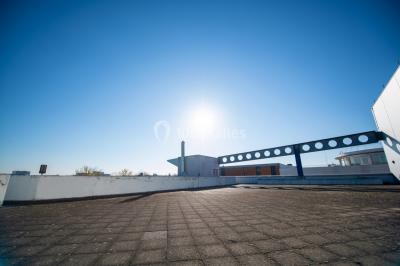 Toit-terrasse ensoleillé avec sol en dalles, balustrade moderne et ciel bleu dégagé en arrière-plan.