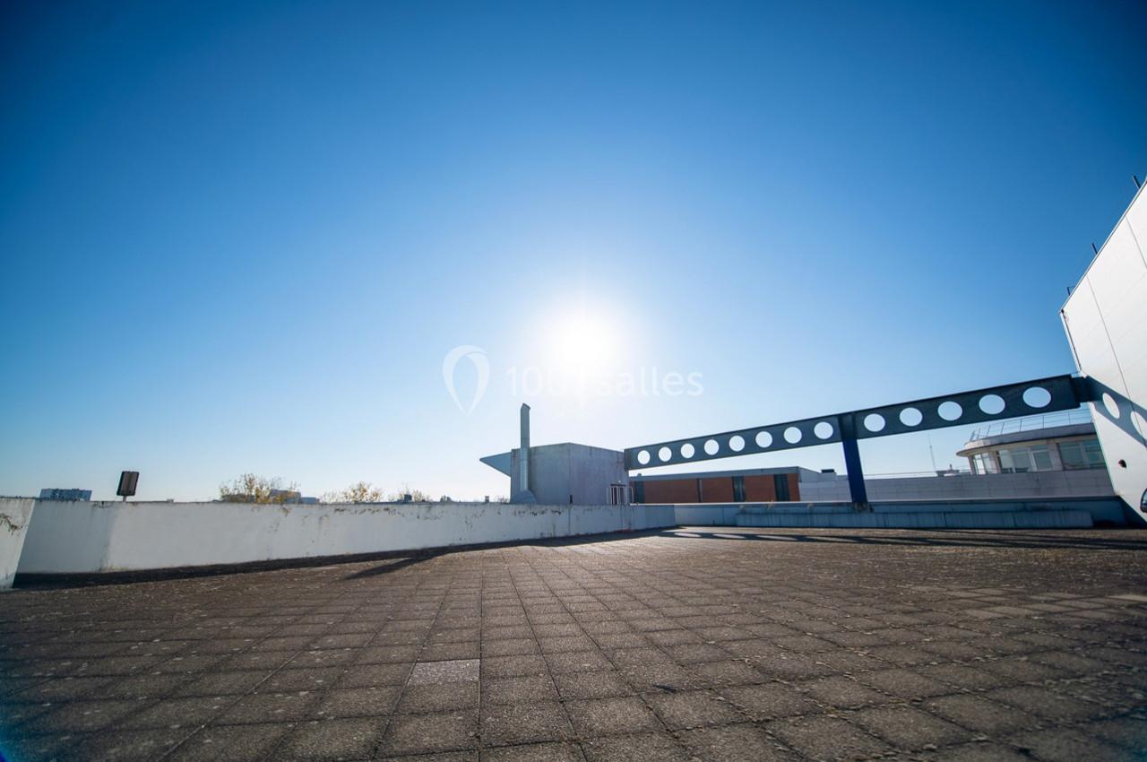 Toit-terrasse ensoleillé avec sol en dalles, balustrade moderne et ciel bleu dégagé en arrière-plan.