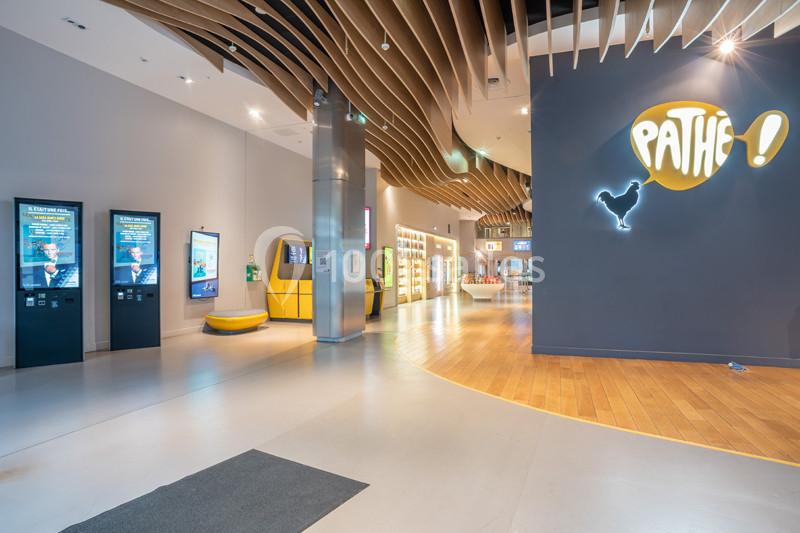 Hall d'entrée d'un cinéma moderne avec bornes interactives, enseigne lumineuse et plafond au design ondulé.