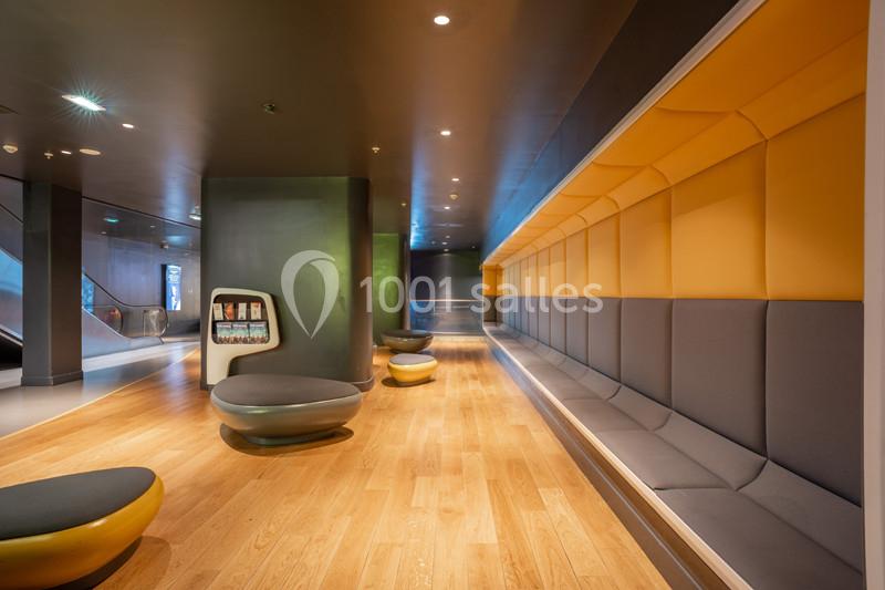 Espace intérieur moderne avec bancs rembourrés jaunes et gris, sol en bois clair et éclairage tamisé.