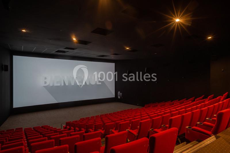 Salle de cinéma vide avec des rangées de fauteuils rouges et un écran affichant le mot ’Bienvenue’.