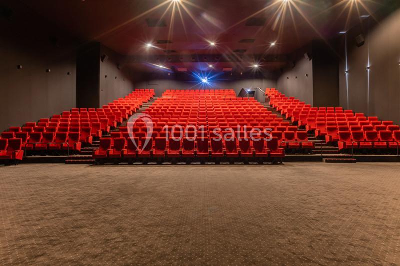 Salle de cinéma vide avec des rangées de sièges rouges alignés et un éclairage tamisé.