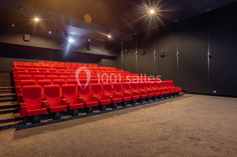 Salle de cinéma vide avec des rangées de fauteuils rouges et un éclairage tamisé.