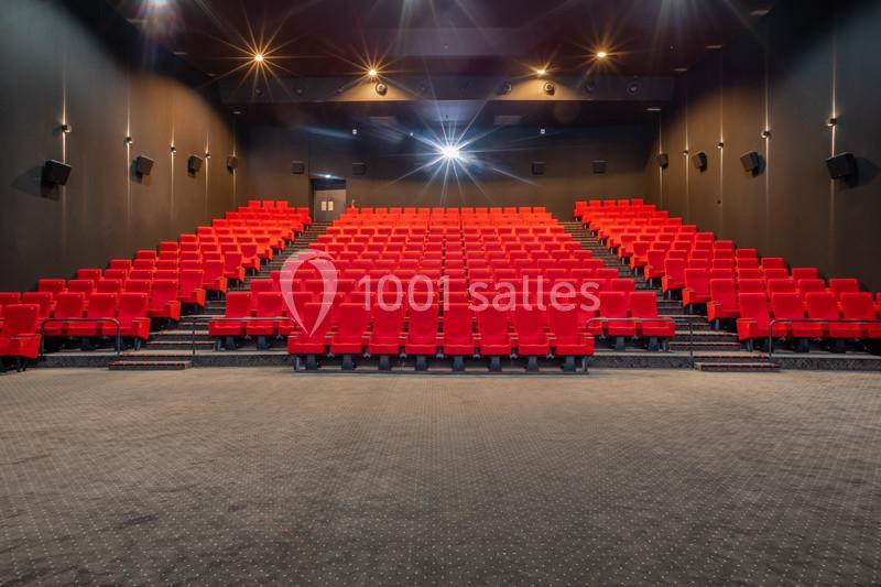 Salle de cinéma vide avec rangées de fauteuils rouges, éclairage tamisé et écran non visible à l'avant.