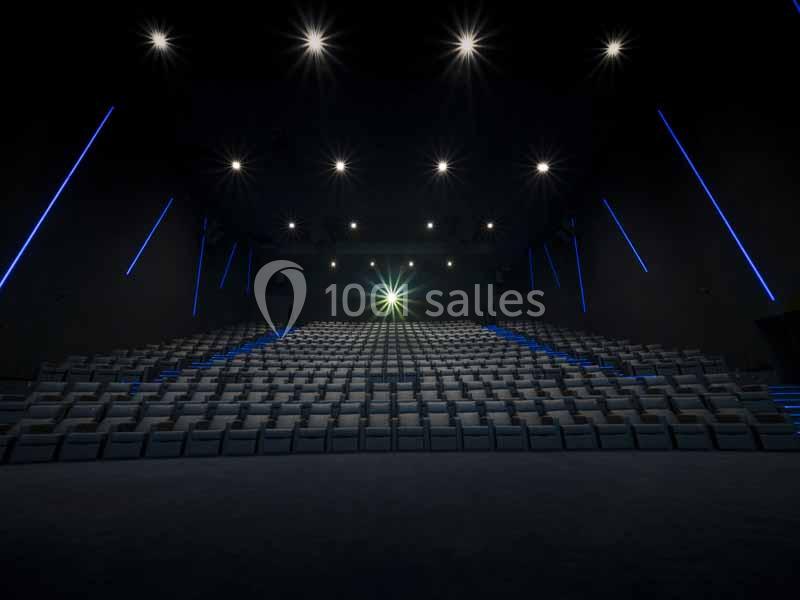 Salle de cinéma vide avec rangées de sièges alignés, éclairage tamisé et projecteur allumé au fond.