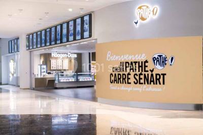 Façade d'un bâtiment moderne avec des enseignes de cinéma IMAX et 4DX, entouré d'une pelouse et d'arbustes.