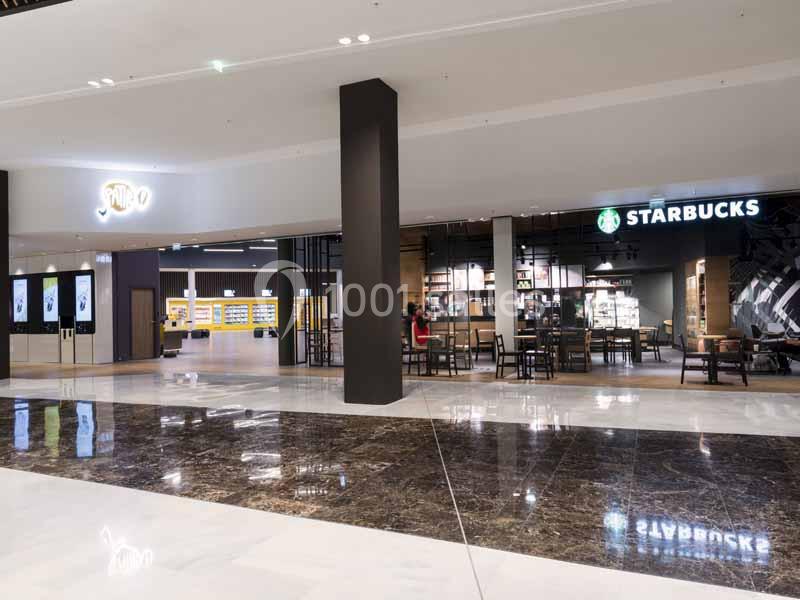Vue d'une galerie commerciale avec un Starbucks et un autre magasin éclairés, tables et chaises disposées devant.