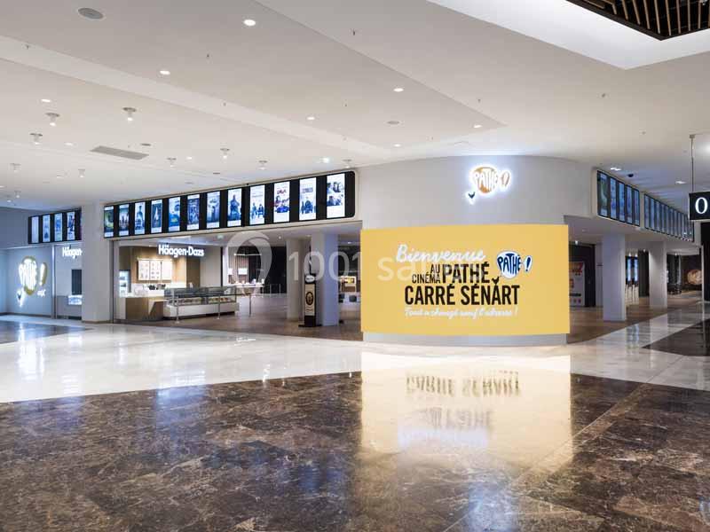Entrée d'un cinéma avec un panneau ’Bienvenue Cinéma Pathé Carré Sénart’, entourée de boutiques et d'écrans d'affichage.