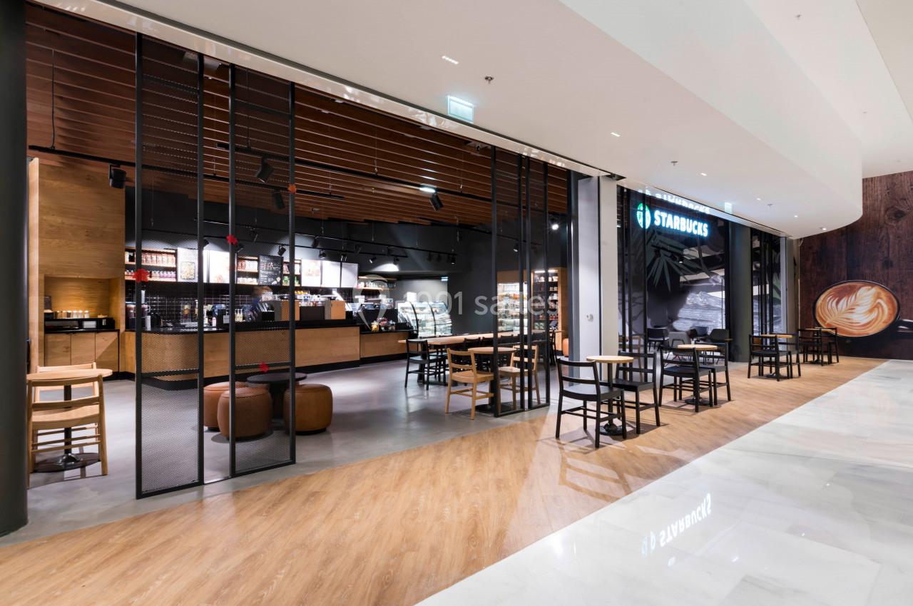 Intérieur d'un café moderne avec comptoir, tables en bois et éclairage chaleureux, situé dans un centre commercial.
