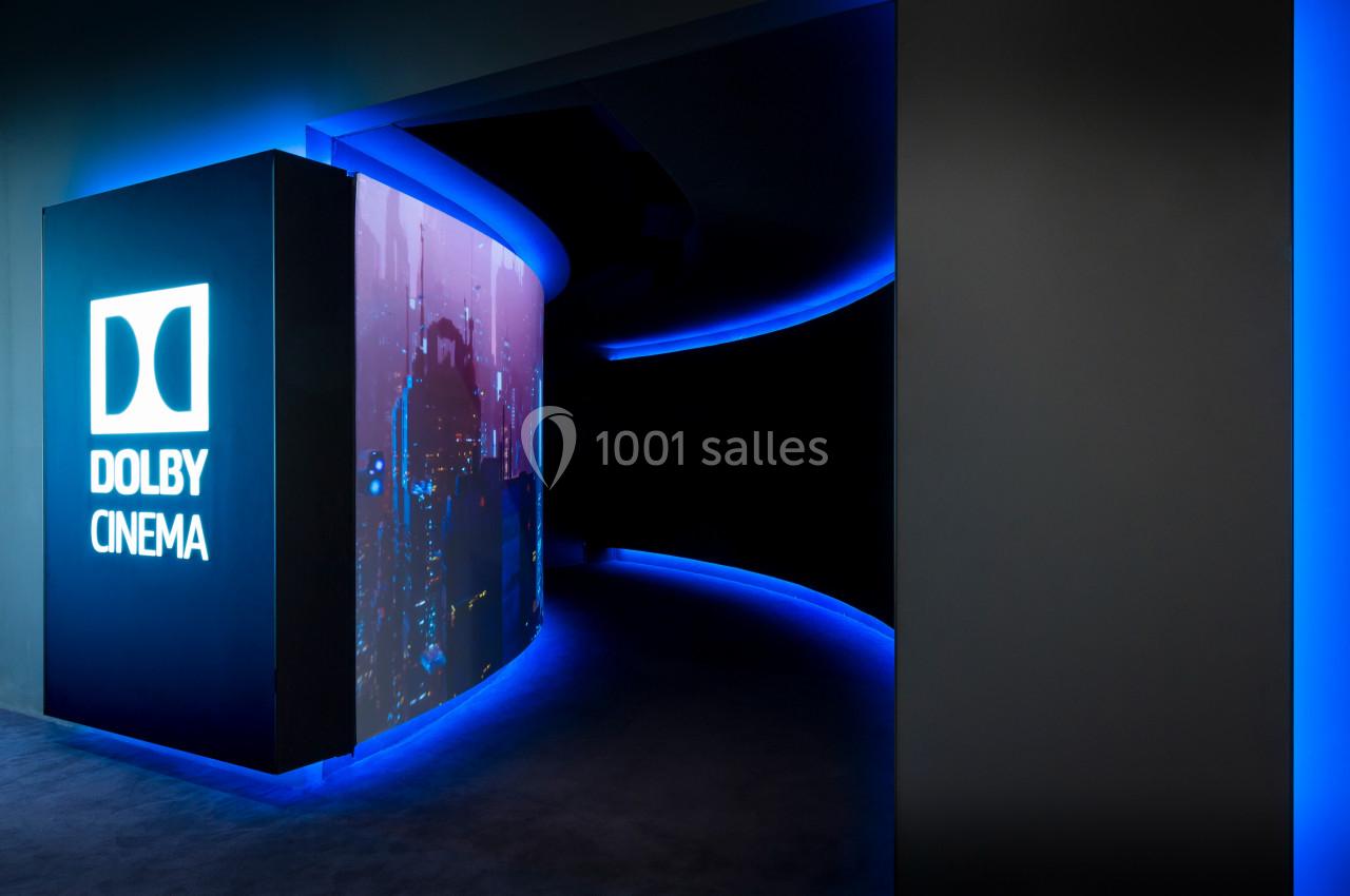 Entrée d'un cinéma Dolby avec un couloir illuminé de lumières bleues et un écran affichant une image urbaine.