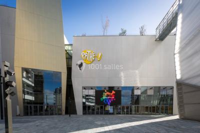 Hall moderne avec bancs, écrans numériques, visiteurs et décorations colorées, incluant une silhouette de coq sur un mur.