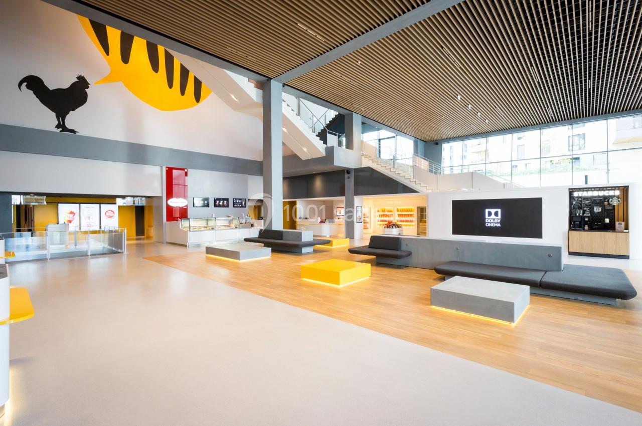 Intérieur d'un espace moderne avec des bancs, un écran mural, un plafond en bois et une décoration murale colorée.