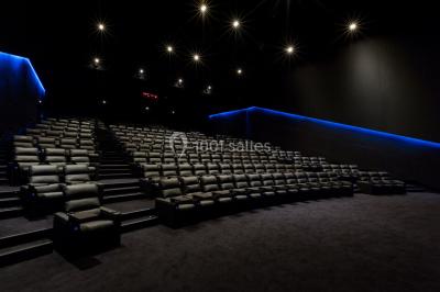 Hall moderne avec bancs, écrans numériques, visiteurs et décorations colorées, incluant une silhouette de coq sur un mur.