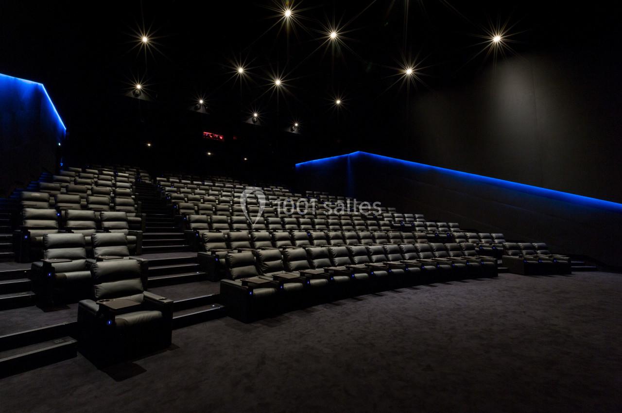 Salle de cinéma vide avec sièges inclinables en rangées et éclairage tamisé bleu sur les murs.