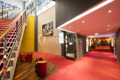 Salle de cinéma vide avec des rangées de sièges rouges et un écran allumé au fond.