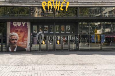 Salle de cinéma vide avec des rangées de sièges rouges et un écran allumé au fond.