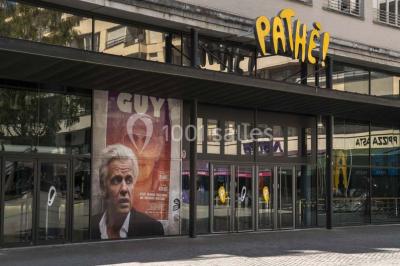Salle de cinéma vide avec des rangées de sièges rouges et un écran allumé au fond.