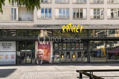 Salle de cinéma vide avec des rangées de sièges rouges et un écran allumé au fond.