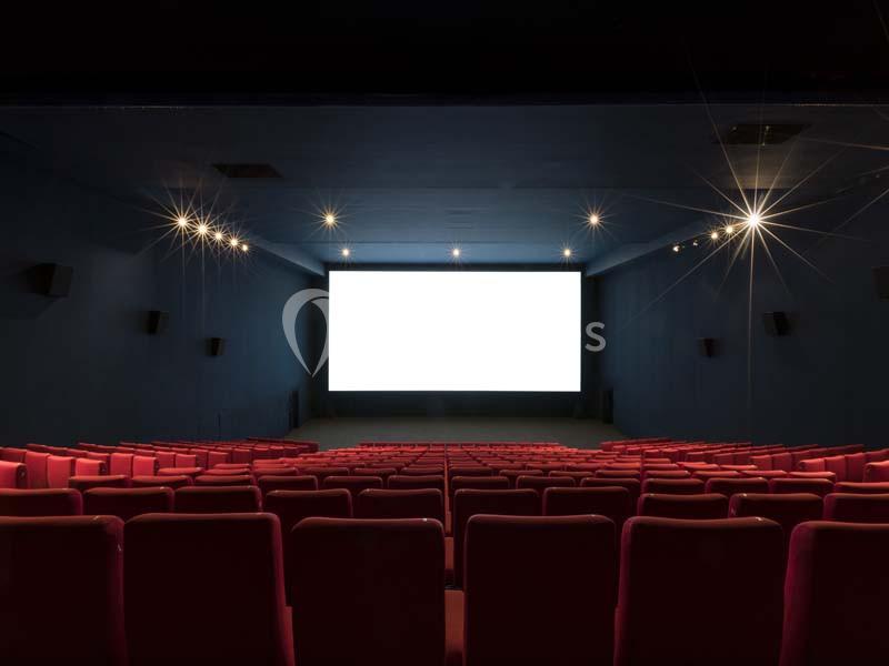 Salle de cinéma vide avec des rangées de sièges rouges et un écran blanc allumé au fond.