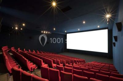 Salle de cinéma vide avec des rangées de sièges rouges et un écran allumé au fond.