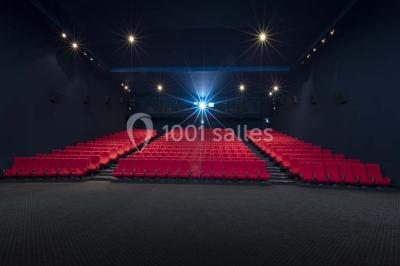 Salle de cinéma vide avec des rangées de sièges rouges et un écran allumé au fond.