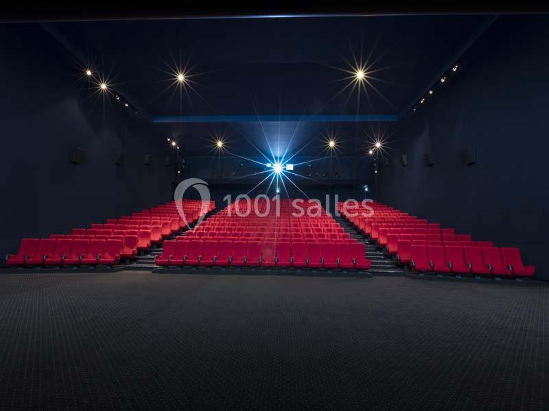 Salle de cinéma vide avec des rangées de sièges rouges et un projecteur allumé au fond.