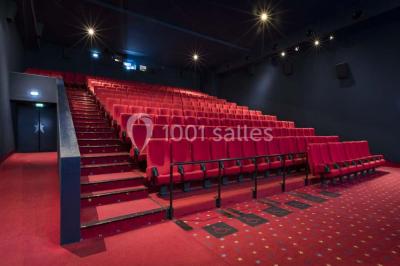 Salle de cinéma vide avec des rangées de sièges rouges et un écran allumé au fond.