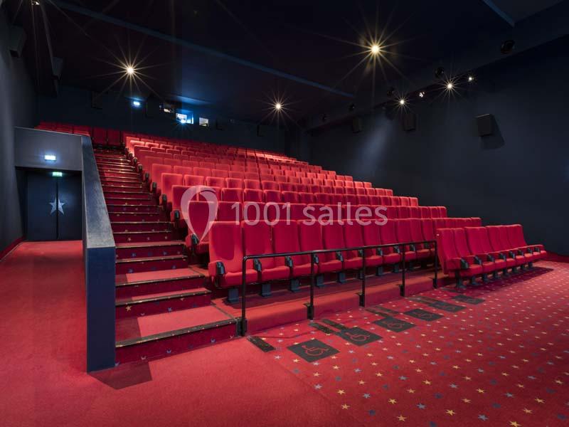 Salle de cinéma vide avec des rangées de sièges rouges et un sol recouvert de moquette rouge à motifs.