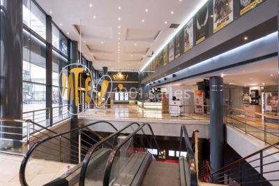 Salle de cinéma vide avec des rangées de sièges rouges et un écran allumé au fond.