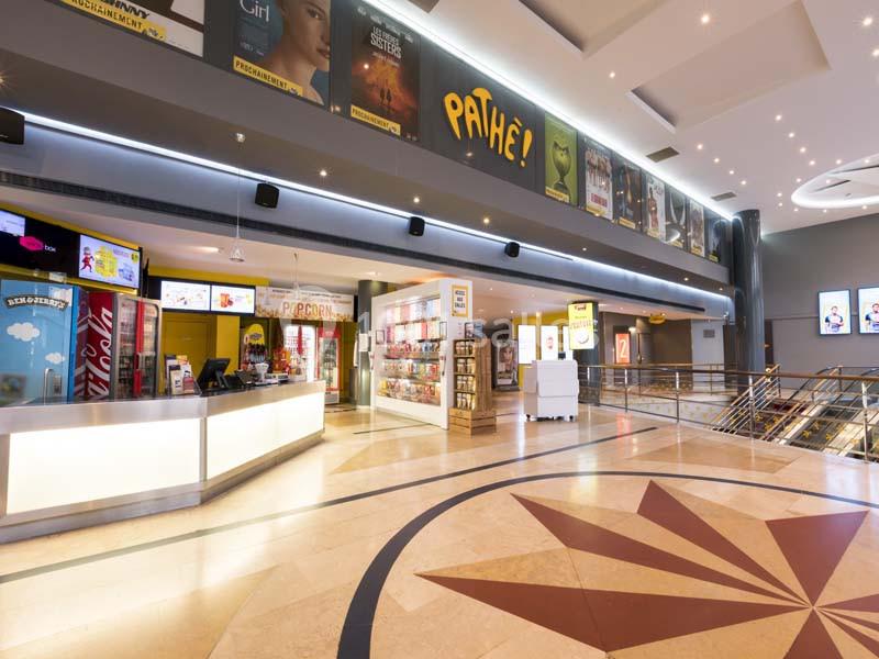 Hall d'entrée lumineux d'un cinéma avec comptoirs de vente, affiches de films et sol en marbre décoratif.