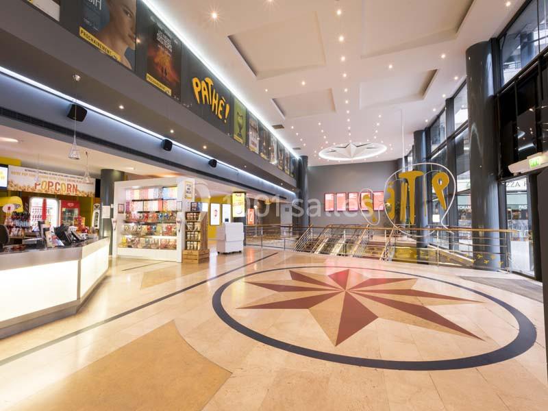 Hall lumineux d'un cinéma avec comptoir de confiseries, escalators et affiches de films sur les murs.