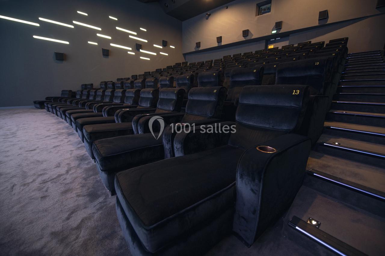 Salle de cinéma moderne avec des rangées de fauteuils noirs rembourrés et des éclairages muraux discrets.