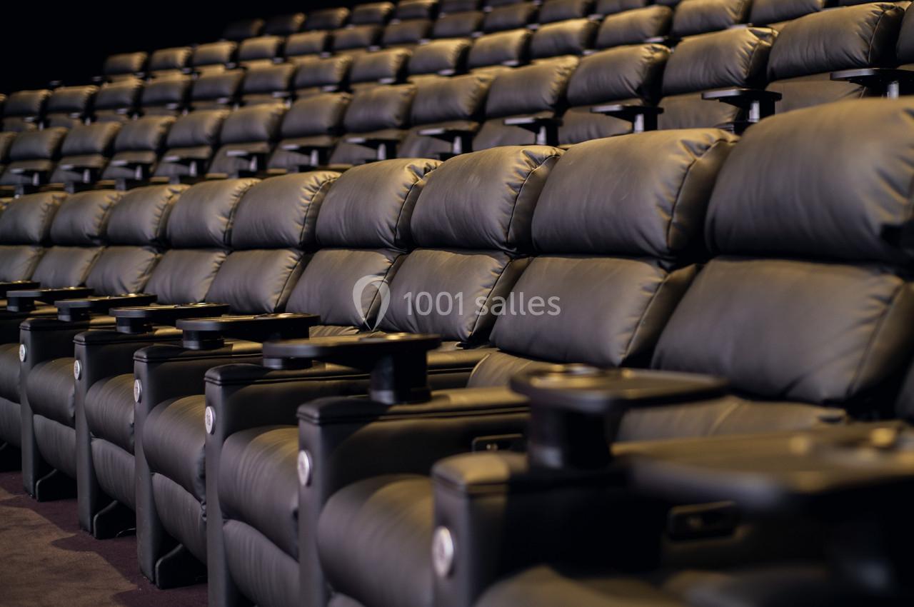 Rangées de fauteuils en cuir noir avec accoudoirs et porte-gobelets dans une salle de cinéma vide.