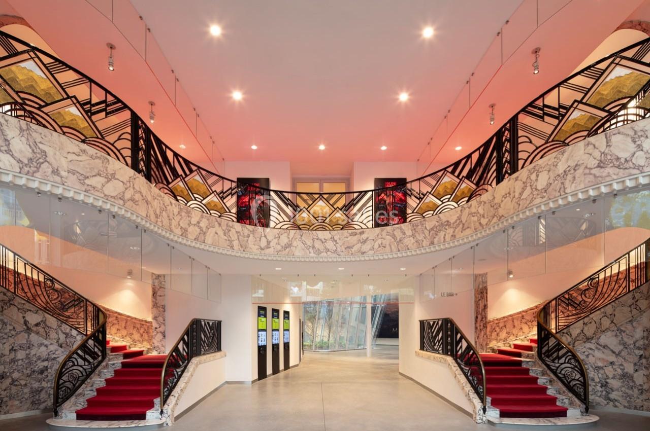 Hall d'entrée avec escalier symétrique, tapis rouge, balustrades décorées et éclairage chaleureux.