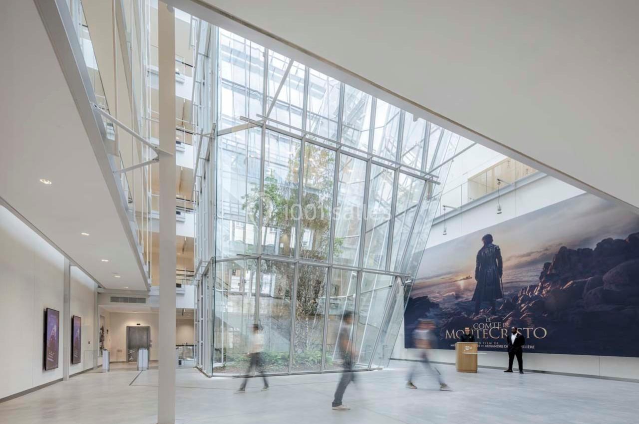 Hall lumineux avec verrière inclinée, plantes au centre et affiche murale représentant un paysage rocheux.
