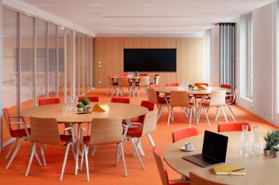 Salle de réunion avec table ronde en bois, chaises rouges, écran mural noir et fournitures de bureau disposées.