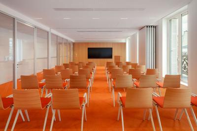 Salle de réunion avec table ronde en bois, chaises rouges, écran mural noir et fournitures de bureau disposées.