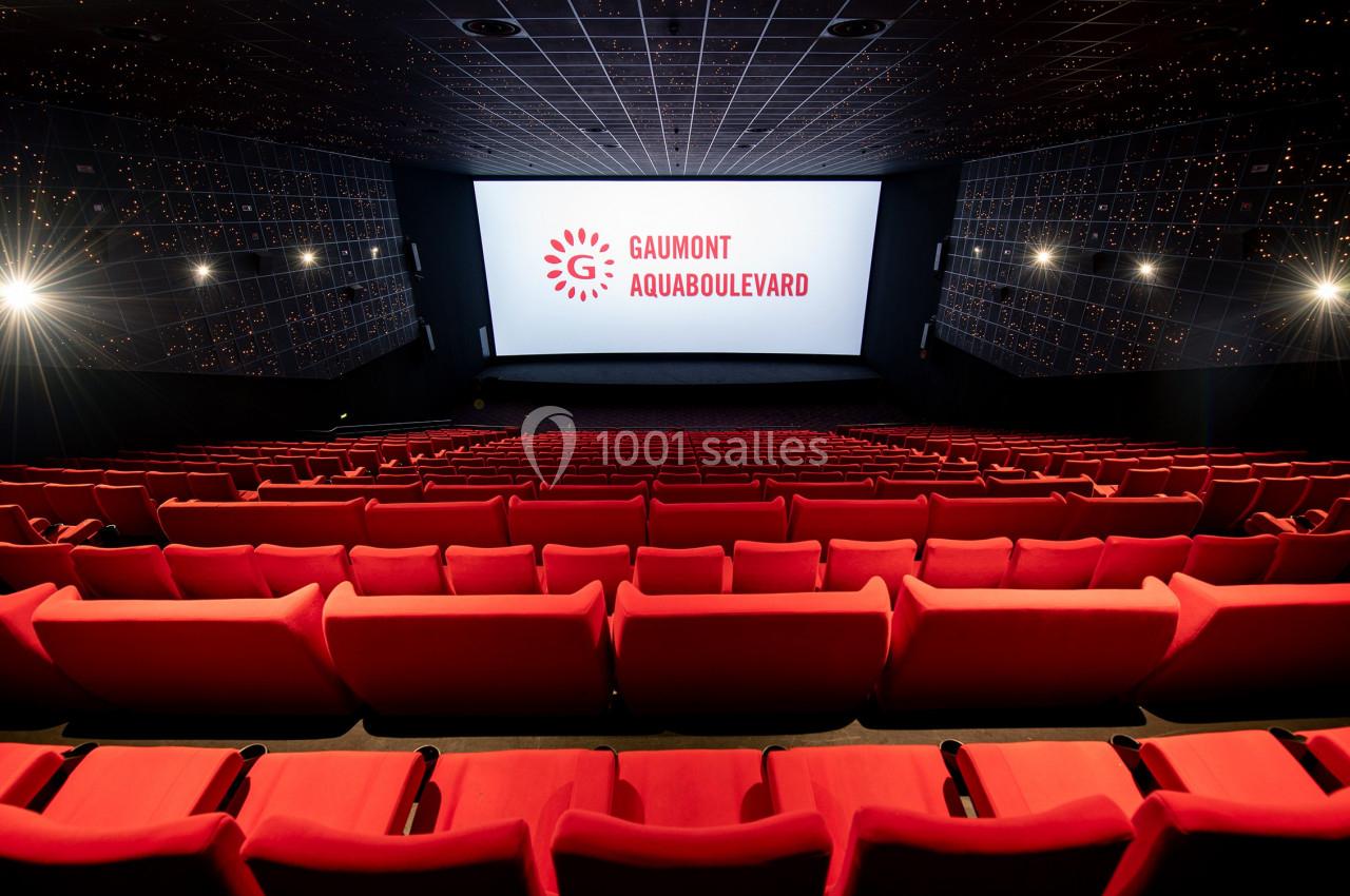 Salle de cinéma vide avec rangées de sièges rouges et écran affichant ’Gaumont Aquaboulevard’.