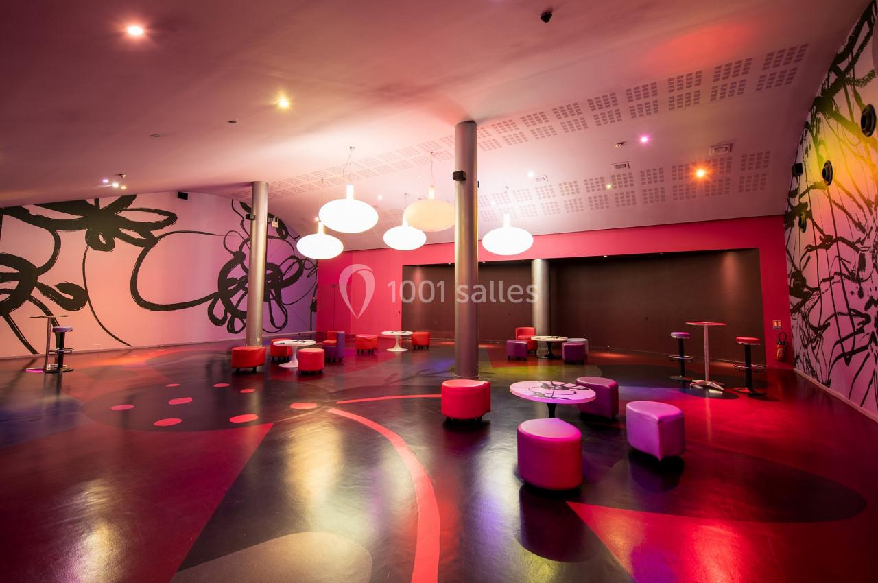 Salle moderne avec murs décorés de motifs floraux, éclairage coloré et mobilier bas, composée de poufs et tables.