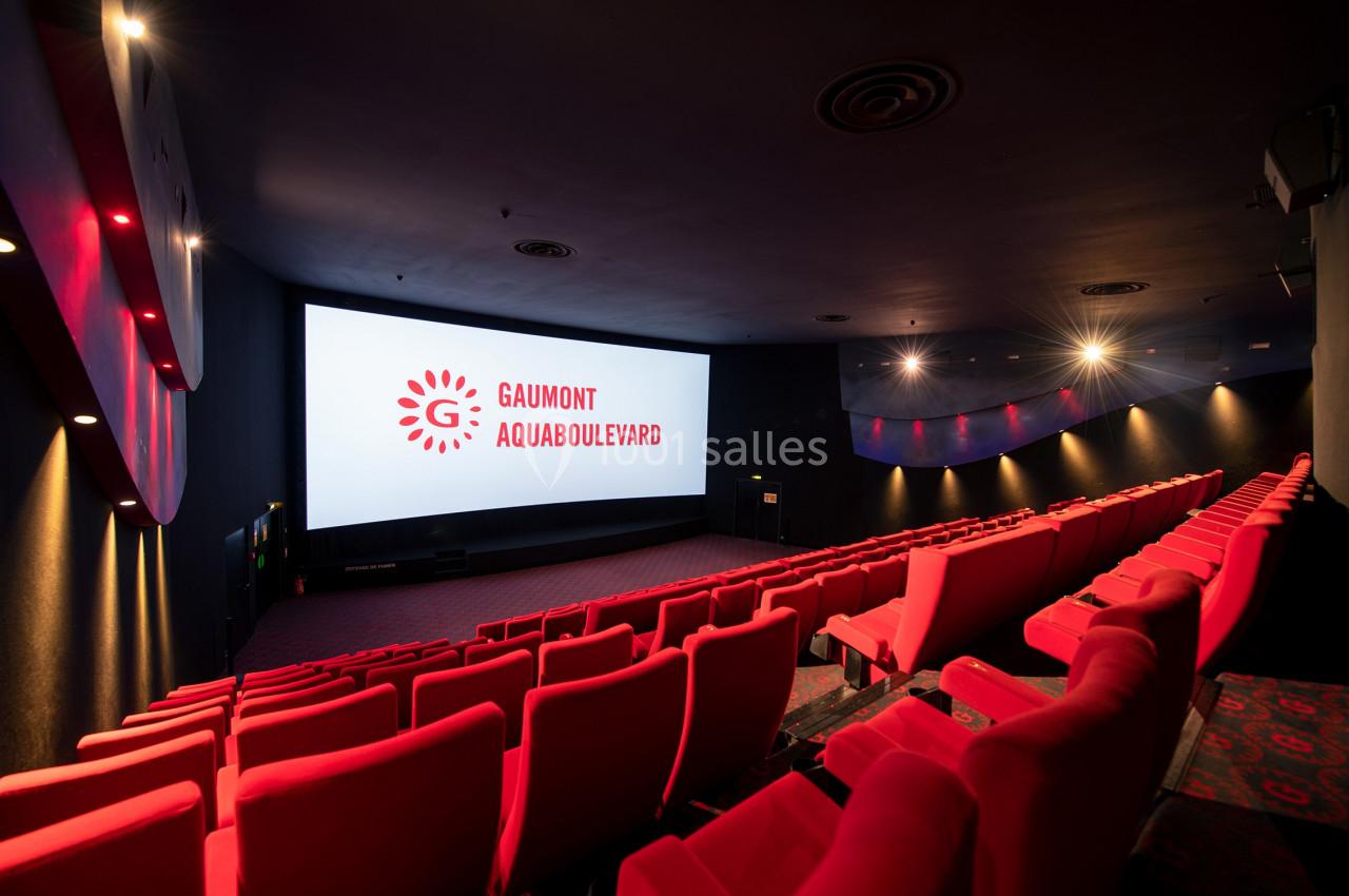 Salle de cinéma vide avec des rangées de sièges rouges et un écran affichant ’Gaumont Aquaboulevard’.