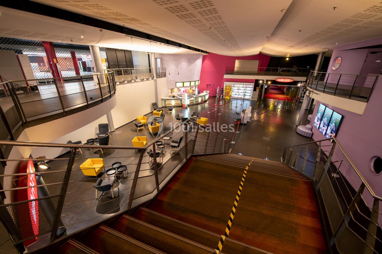 Vue intérieure d'un espace public moderne avec escalier central, sièges colorés et comptoirs de restauration.
