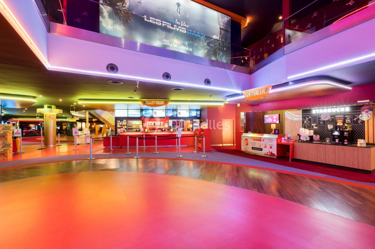 Hall de cinéma lumineux avec comptoirs de billetterie et de confiserie, affiches de films en arrière-plan.