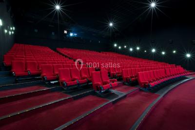 Salle de cinéma vide avec des rangées de sièges rouges et un écran éteint à l'arrière-plan.
