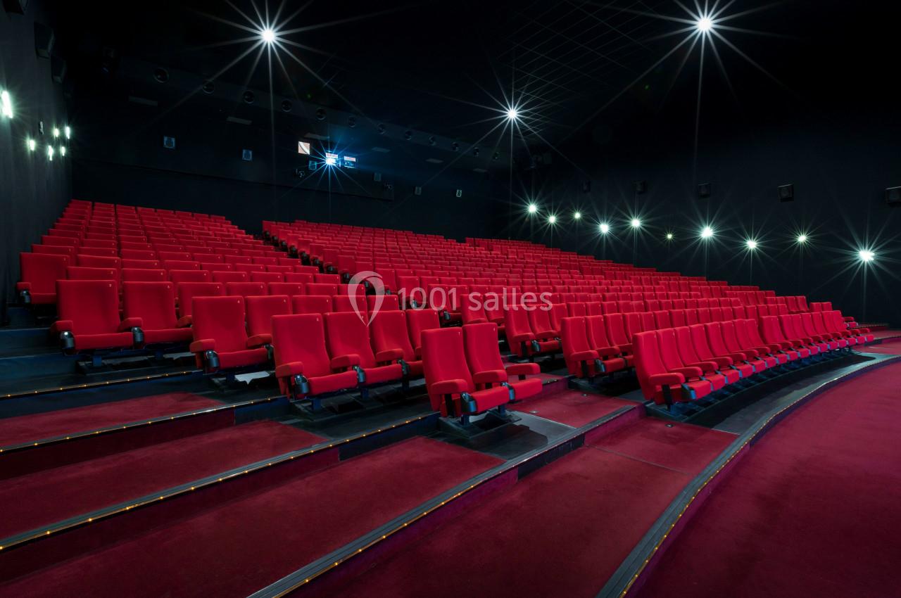 Salle de cinéma vide avec des rangées de sièges rouges et un écran éteint à l'arrière-plan.