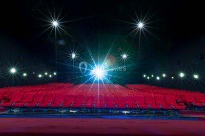 Salle de cinéma vide avec des rangées de sièges rouges et un écran éteint à l'arrière-plan.