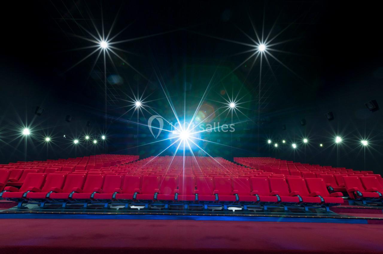 Salle de cinéma vide avec des rangées de sièges rouges et un projecteur allumé au fond.
