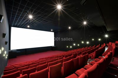 Salle de cinéma vide avec des rangées de sièges rouges et un écran éteint à l'arrière-plan.
