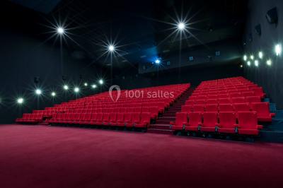 Salle de cinéma vide avec des rangées de sièges rouges et un écran éteint à l'arrière-plan.