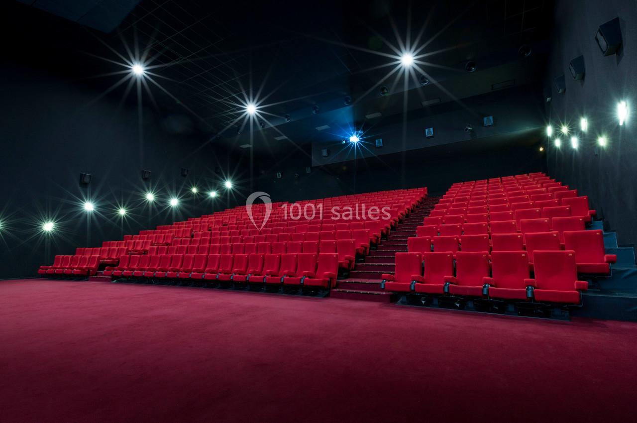 Salle de cinéma vide avec des rangées de sièges rouges et un éclairage tamisé.