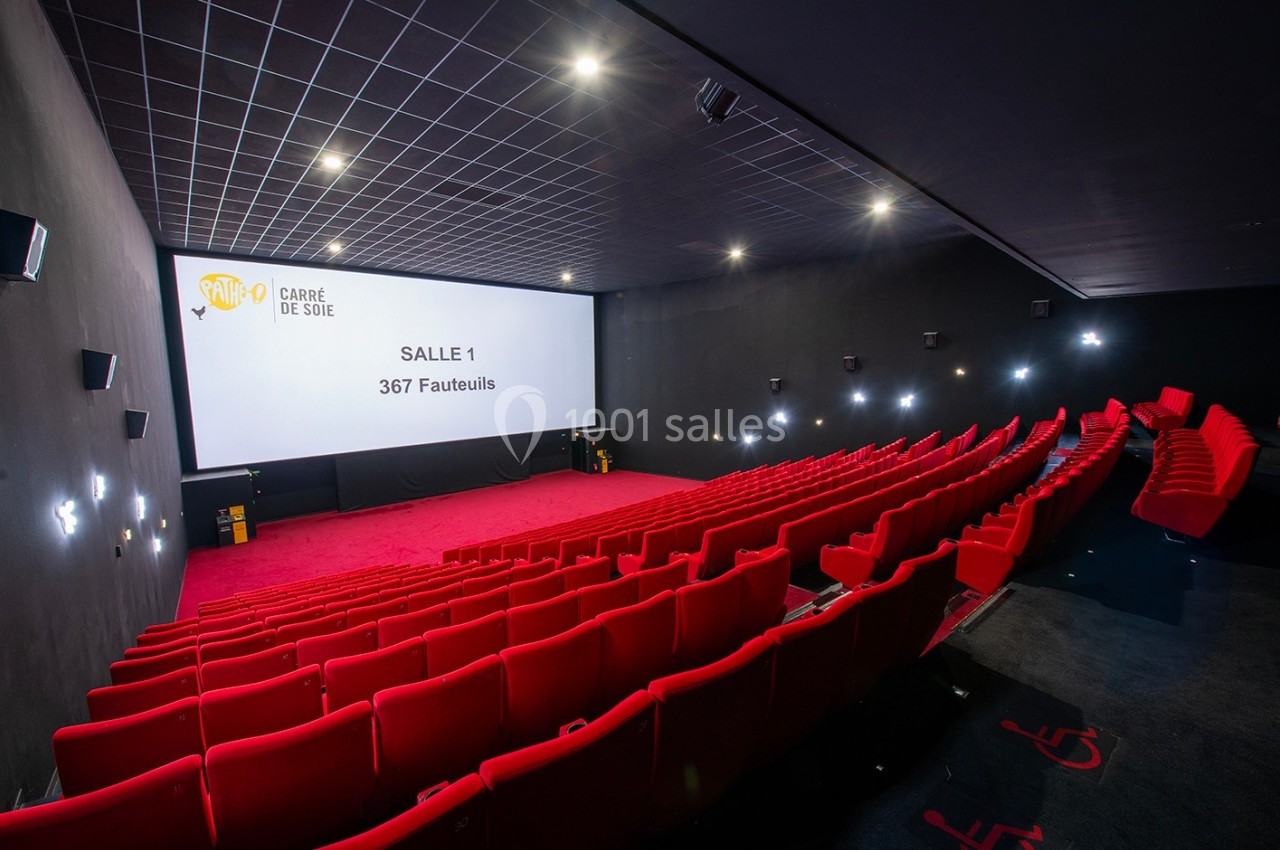 Salle de cinéma moderne avec des rangées de fauteuils rouges et un grand écran affichant des informations sur la salle.